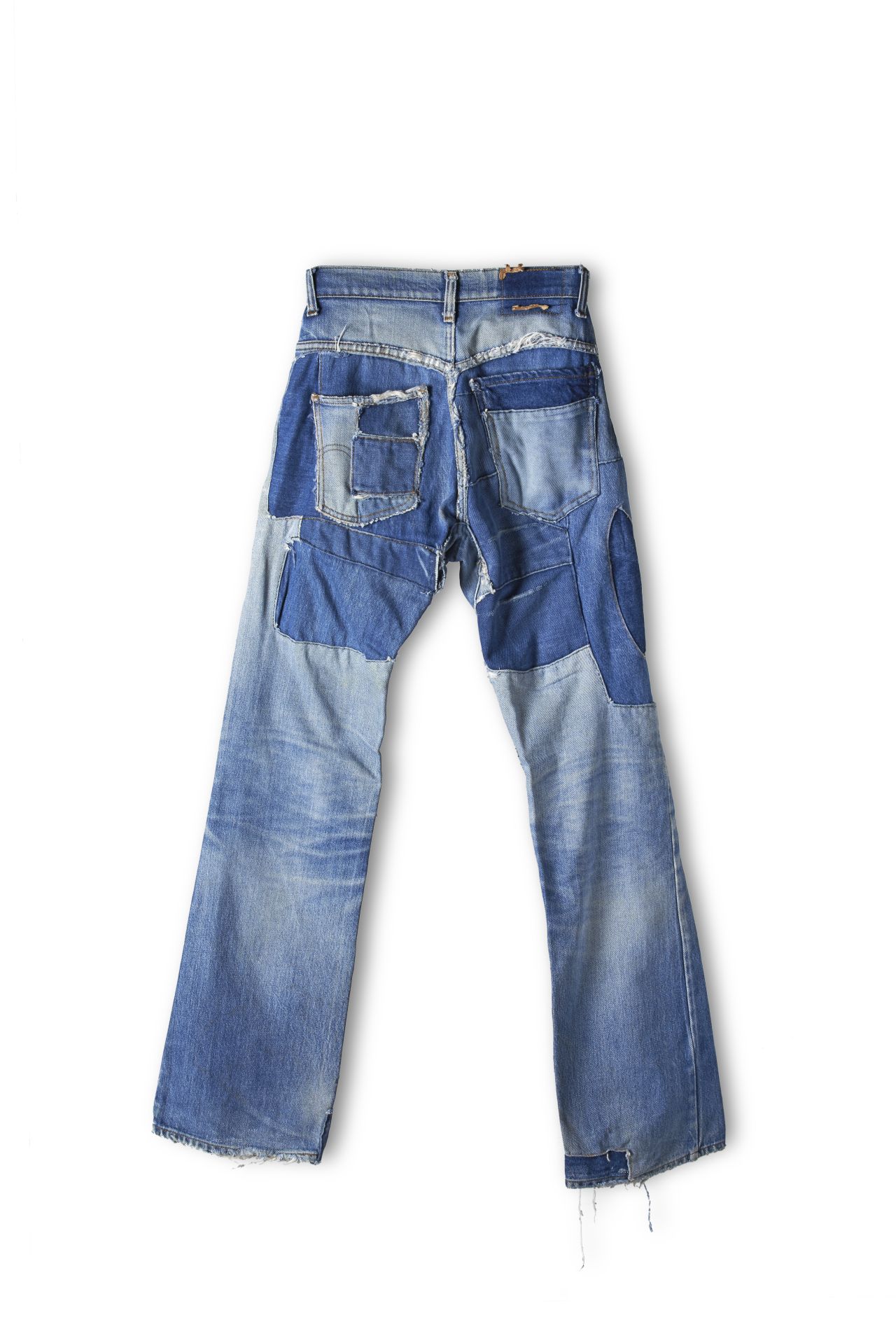 Blaue Jeanshose mit 5 Taschen, viele auf- und eingenähte Jeansflecken in unterschiedlichen Blautönen im Bereich der Oberschenkel, Knie und des Saums.