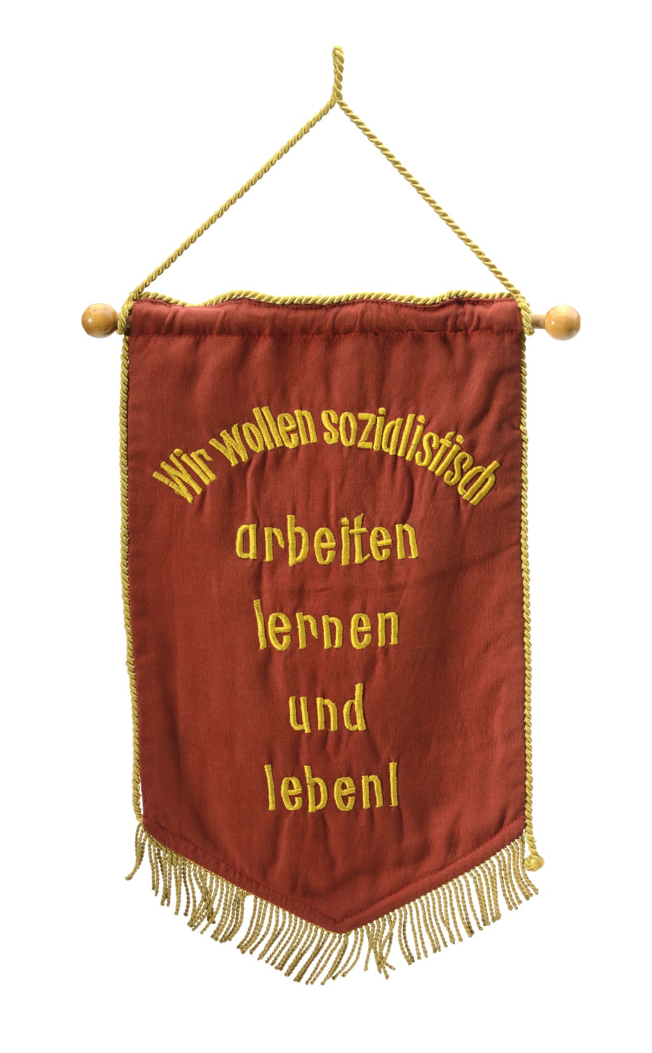 Roter Wimpel umlaufend mit goldfarbener Fransenkordel, beide Seiten unterschiedlich bestickt. Auf dieser Seite Text: Wir wollen sozialistisch arbeiten lernen und leben!