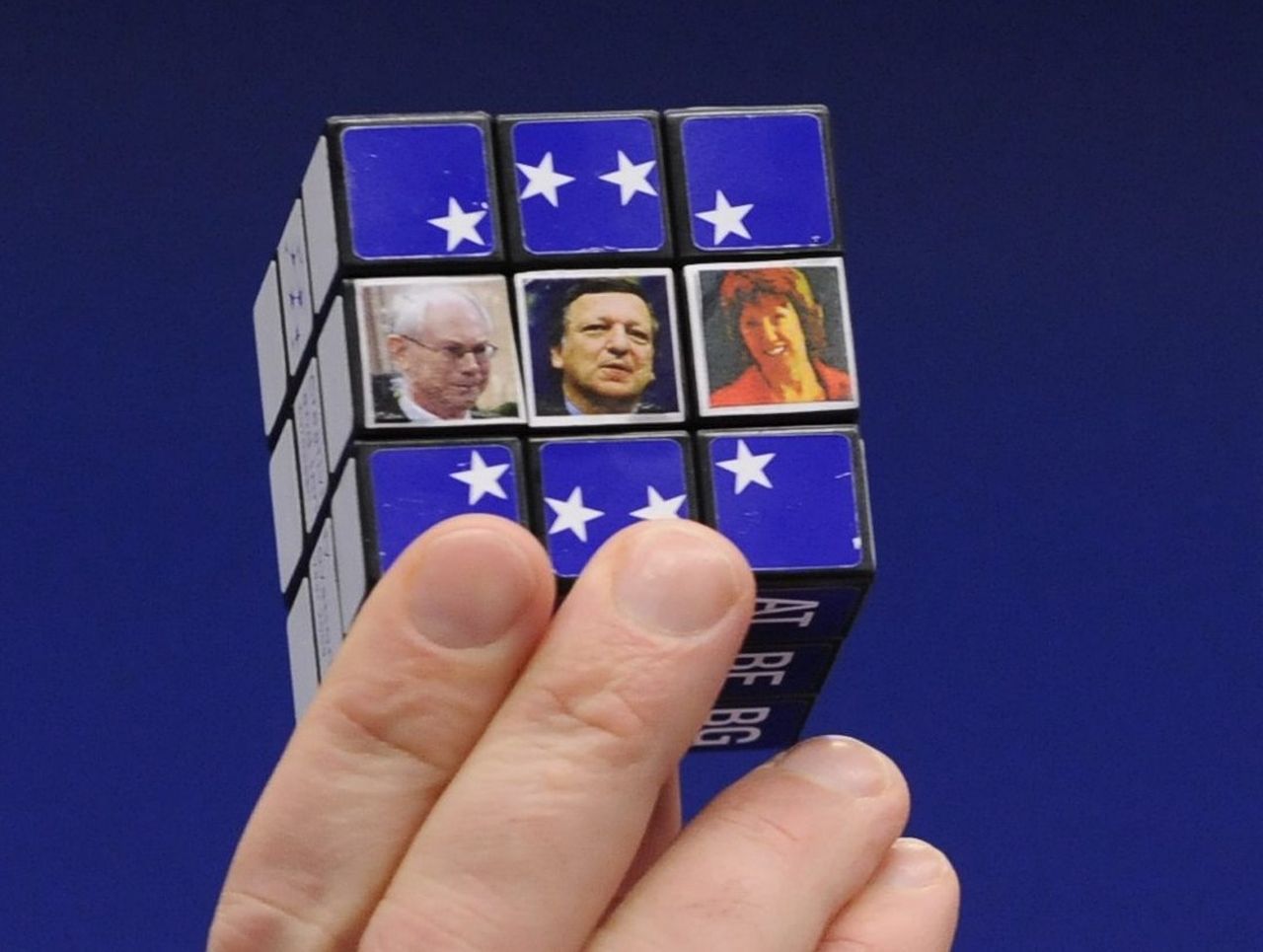 Großansicht eines Rubik-Würfels in einer Hand. In den neun Kästchen des Würfels, die man in der Vorderansicht sieht, sind in der oberen und unteren Zeile weiße EU-Sterne auf blauem Hintergrund zu sehen. Die drei Kästchen der mittleren Reihe zeigen Bilder von Herman van Rompuy, Jose Manuel Barroso und Catherine Ashton.