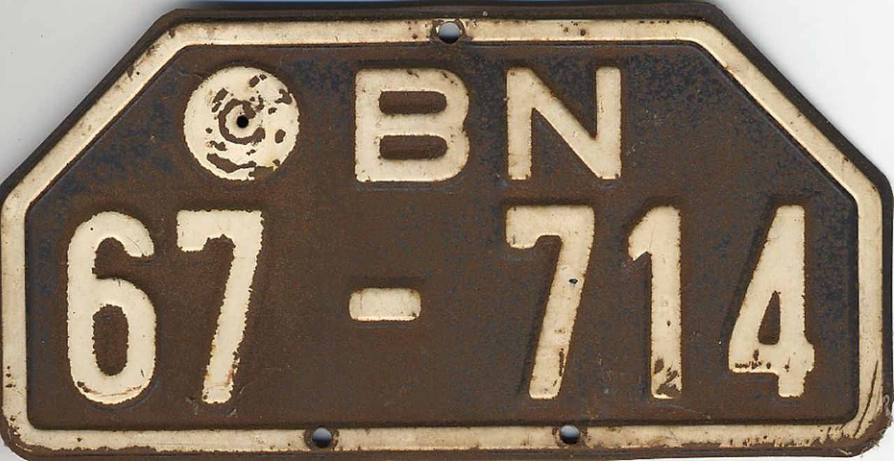 Motorrad-Nummernschild aus der britischen Besatzungszone mit der Aufschrift BN 67-714. Rechteckiges Schild, die oberen Ecken abgeschrägt. Weißer Rand und Schrift auf schwarzem (stark korrodiertem) Grund, drei Befestigungslöcher.